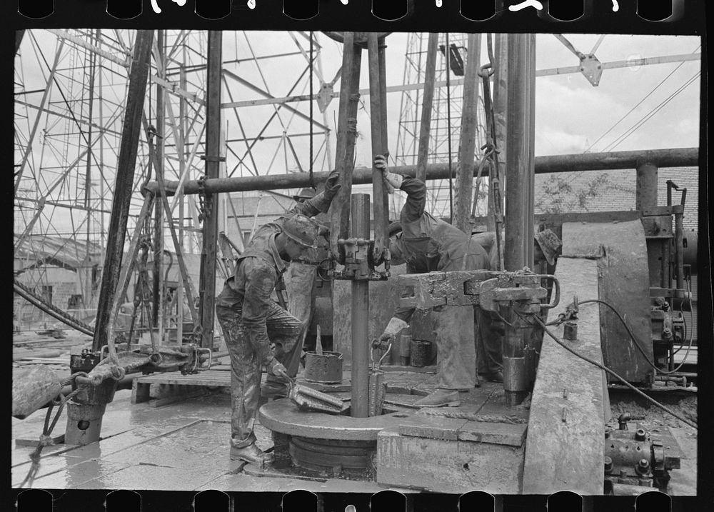 Removing length of pipe from oil well, Kilgore, Texas. Clamps being removed from rotary table and pipe will be elevated by…