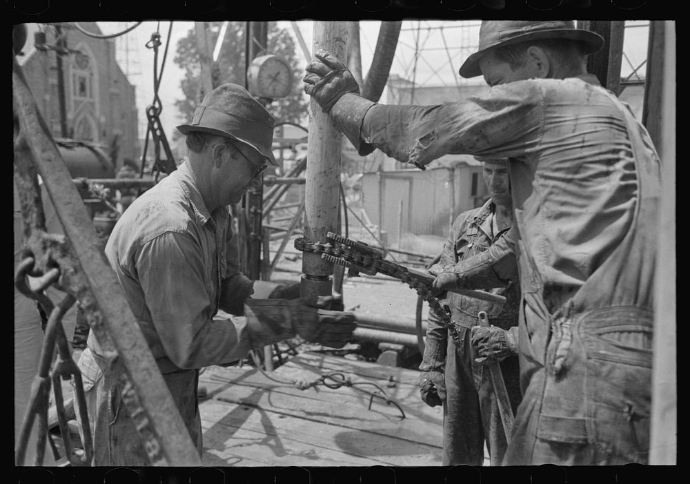 Oil field worker screwing nipple on end of drill stem for test to determine direction and draft of drilling operations…