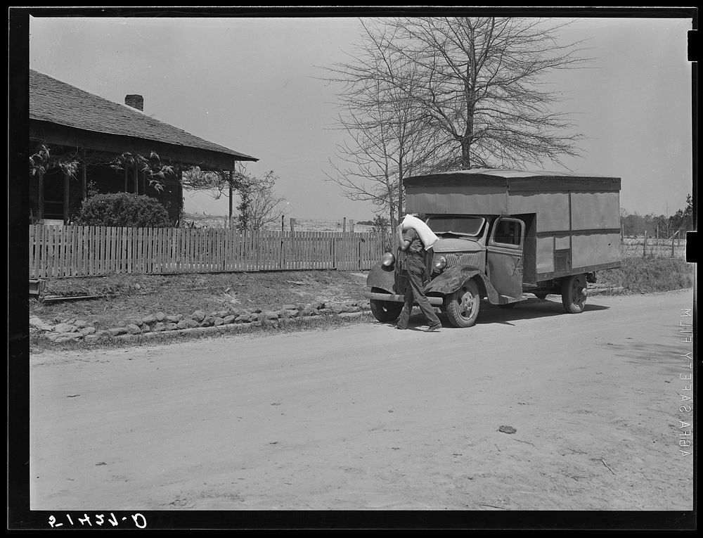 A "rolling store" salesman carrying sack of flour into rural home. Coffee County, Alabama. Sourced from the Library of…