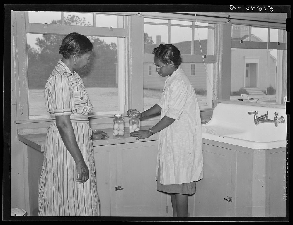 Juanita Coleman, NYA (National Youth Administration) leader and teacher, helps Sally Titus preserve some eggs. Through this…