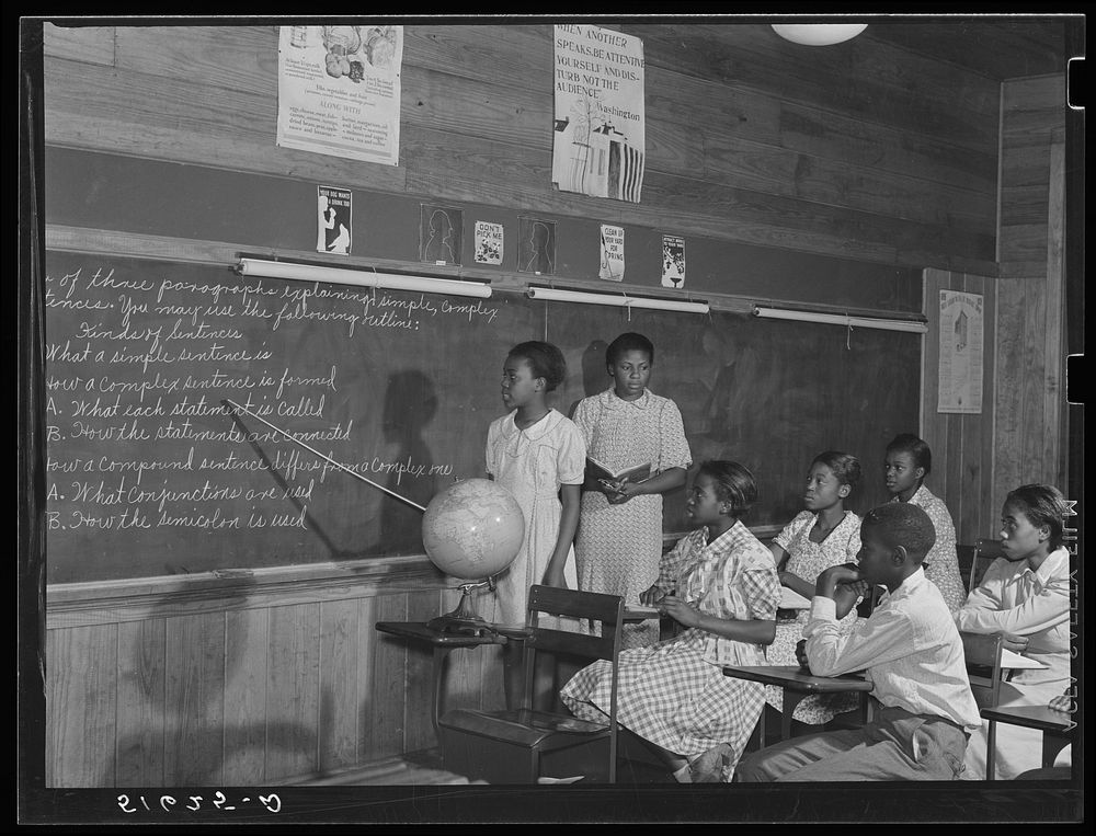 English lesson in sixth and seventh grade school room. Selma Sutton at board with teacher, Miss Jessie West Greene. Flint…