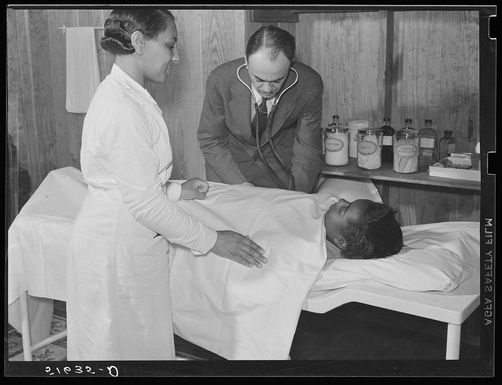 Project nurse Lillie Mae McCormick assists Dr. Thomas M. Adams as he takes Annie Maude Daniels' blood pressure on table in…