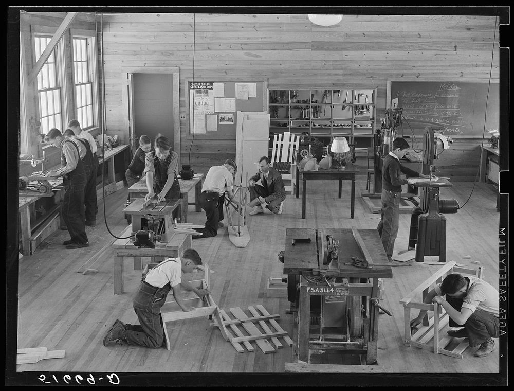 Part of shop class in school with Robert Gentry, teacher, in center kneeling next to boy who is making ironing board.…
