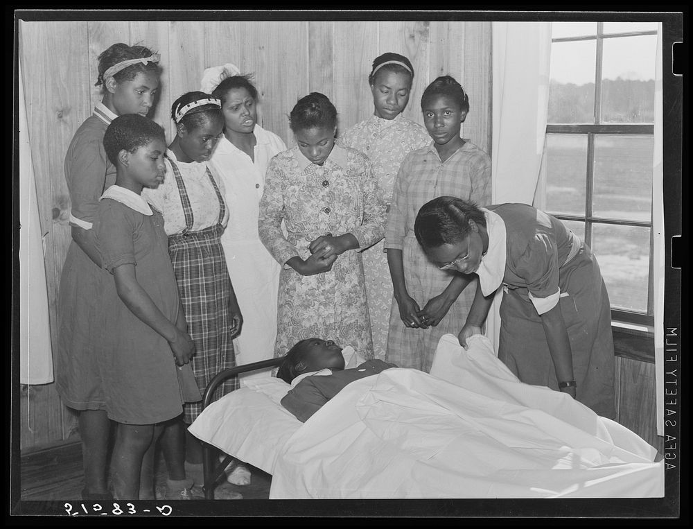 Nurse Shamburg directs group of girls in making sick bed in clinic. Gee's Bend, Alabama. Sourced from the Library of…