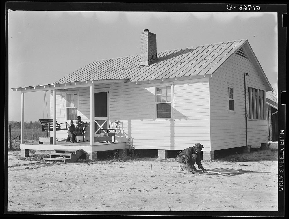 Front of new home of project family. He is building a gate for front yard. Prairie Farms, Alabama. Sourced from the Library…