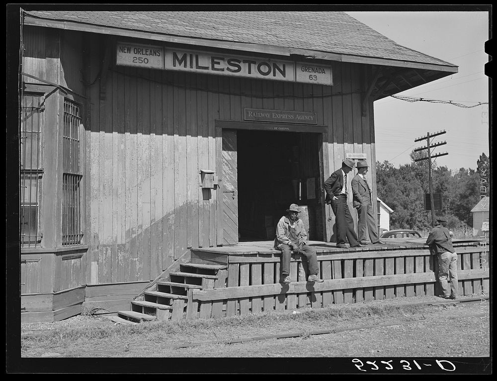 The railway station at Mileston Plantation is the social gathering place. On the platform are the station agent and the…