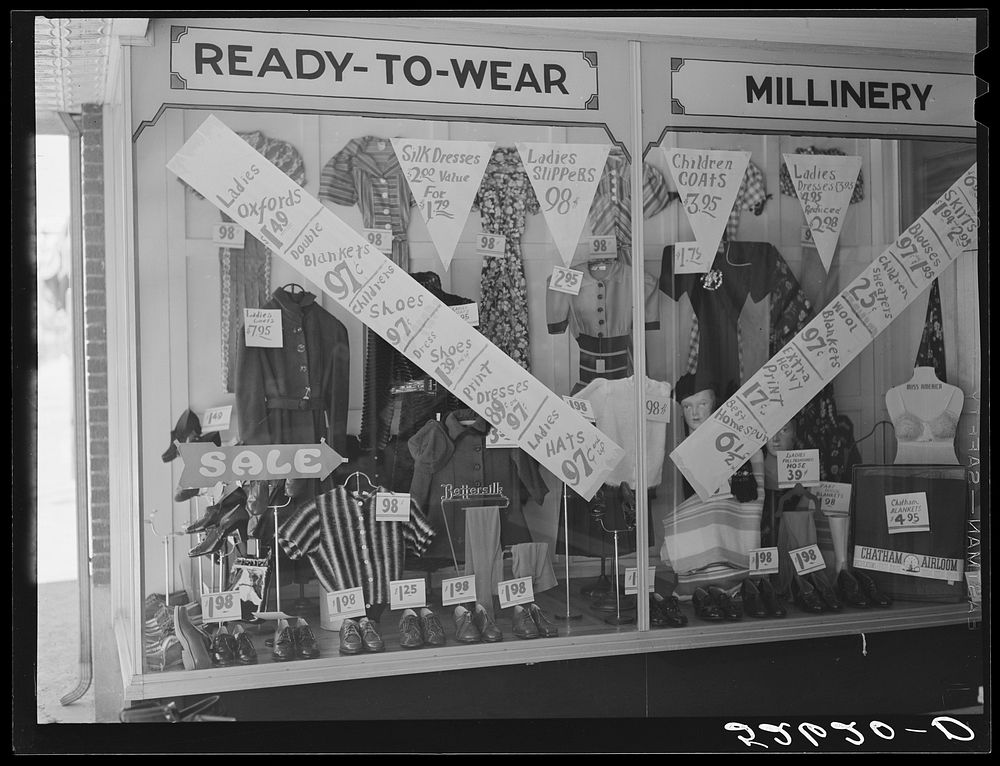 Signs on store window advertising sales during tobacco auction time in Zebulon. Wake County, North Carolina. Sourced from…