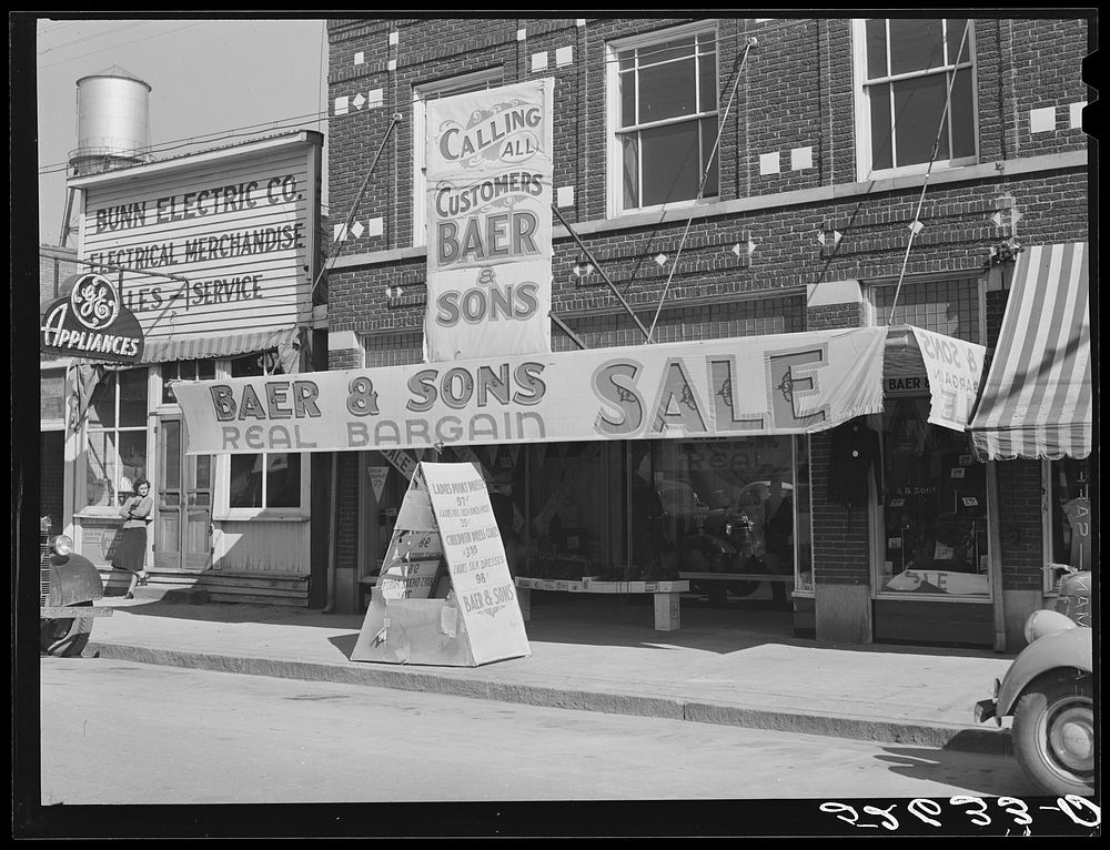 Signs on store window advertising sales during tobacco auction time in Wake County. Zebulon, North Carolina. Sourced from…