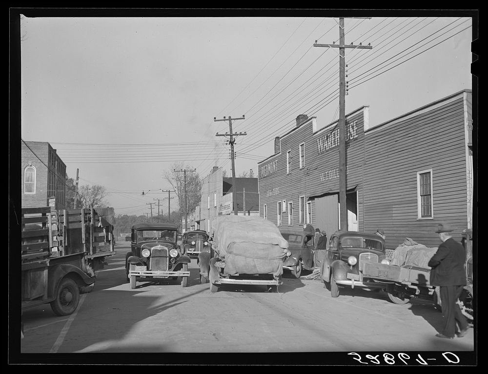 Street showing several tobacco warehouses on day of auction sales with farmers bringing in their tobacco on trailers and…