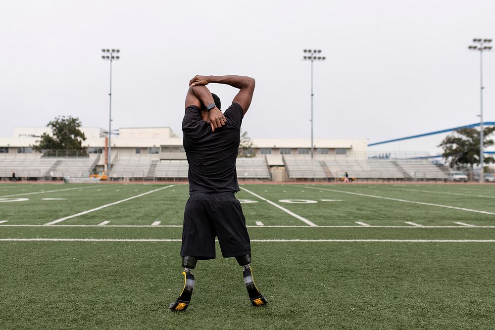 Paralympic athlete with prosthetic legs warming up by stretching before exercising