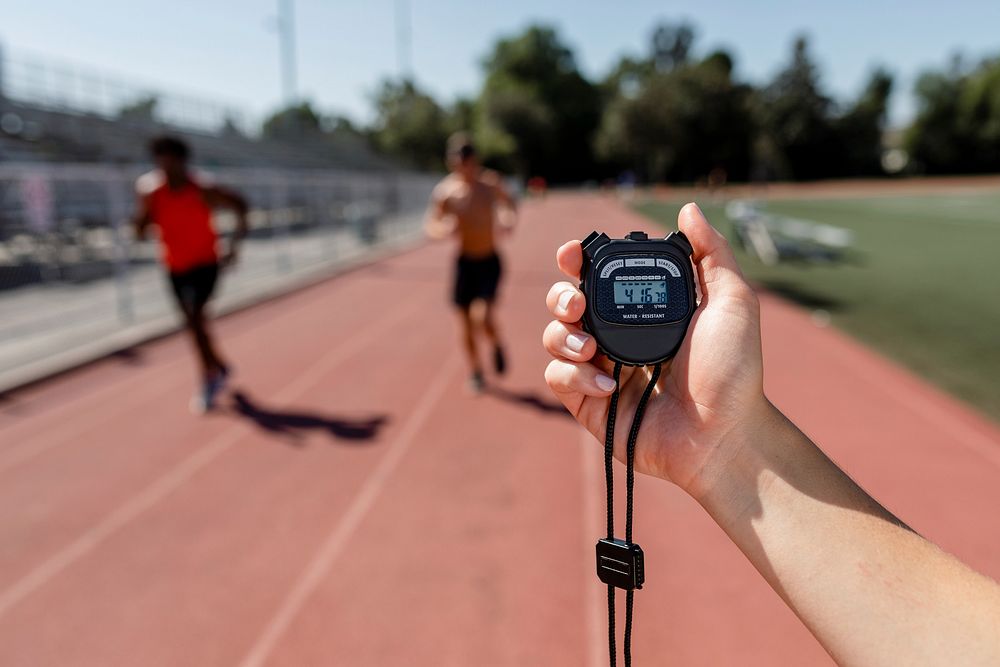 Hand holding stopwatch by a running track