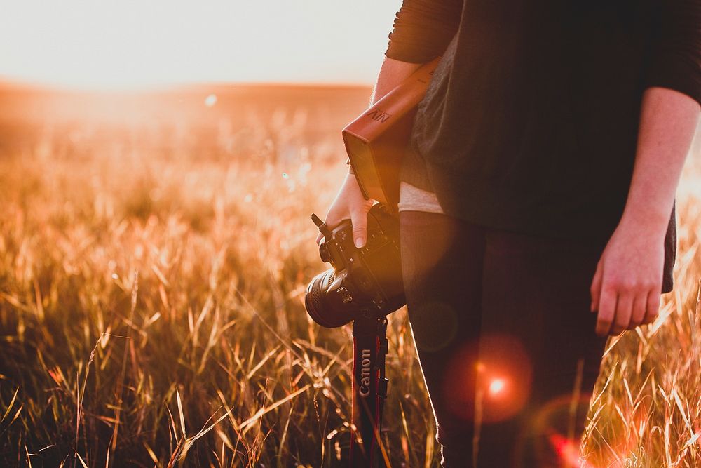 Free man holding camera and book during sunset in field photo, public domain CC0 image.
