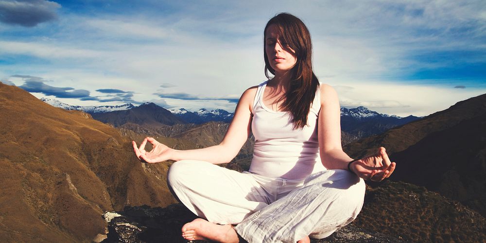 Young woman meditating in the wilderness with beautiful mountain range as a background.