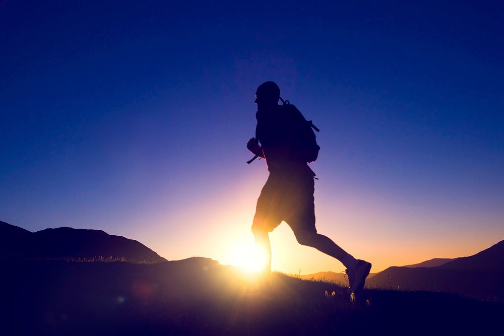 Man's silhouette running in a sunset with mountain range as a background.