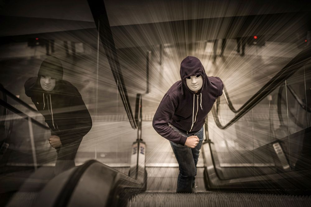 Free man in white mask and hoodie standing on escalator photo, public domain CC0 image.
