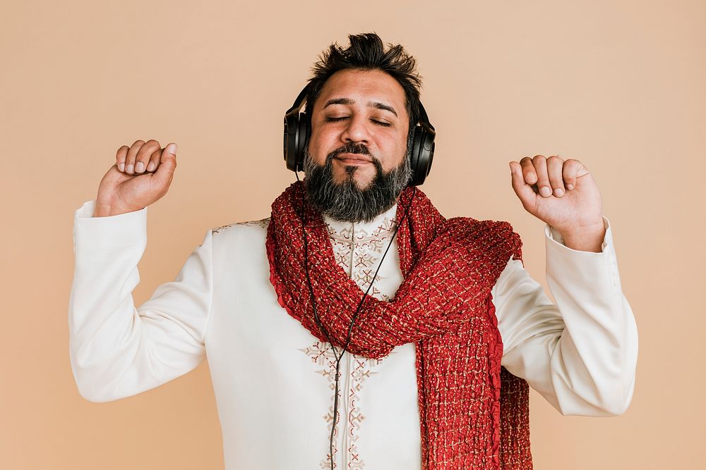 Indian man in a kurta listening to music with headphones 