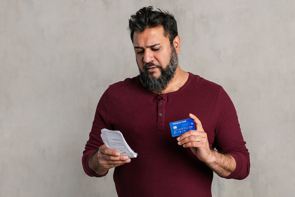 Stressed senior Indian man holding his bills and credit card 