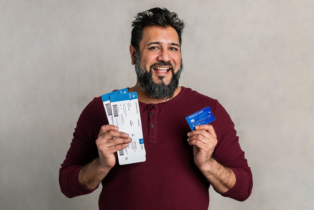 Excited Indian man holding a credit card and flight tickets