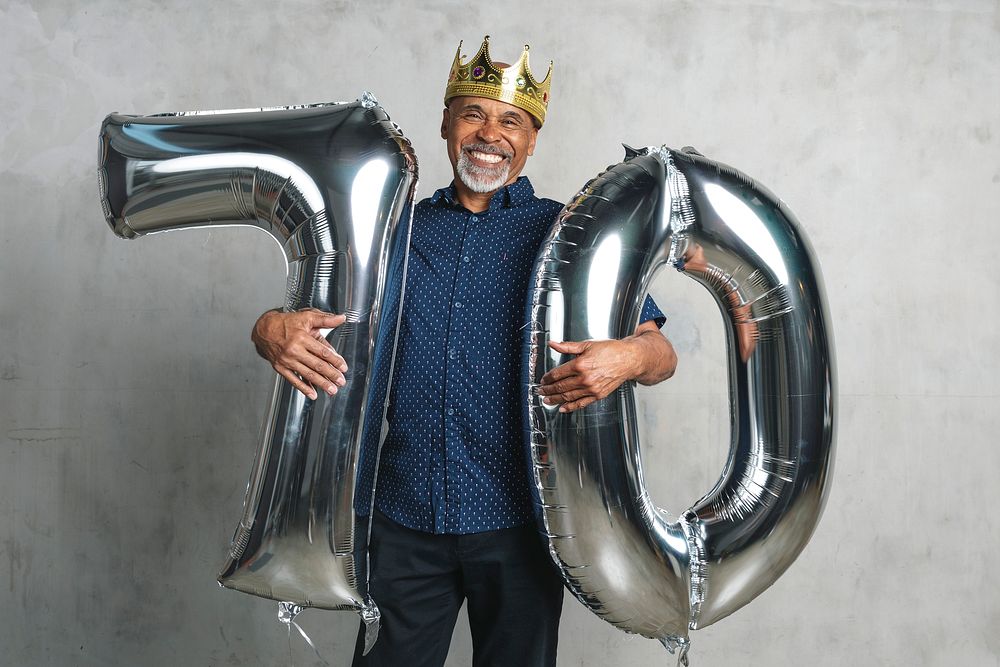 Cheerful senior man holding silver balloons for his 70th birthday celebration