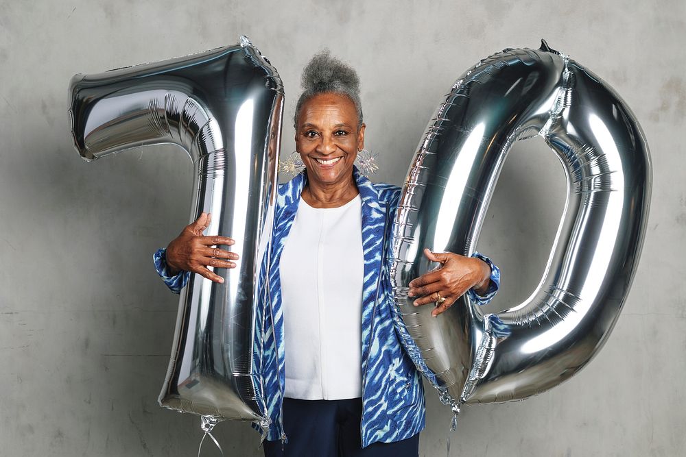Cheerful senior woman holding silver balloons for her 70th birthday celebration