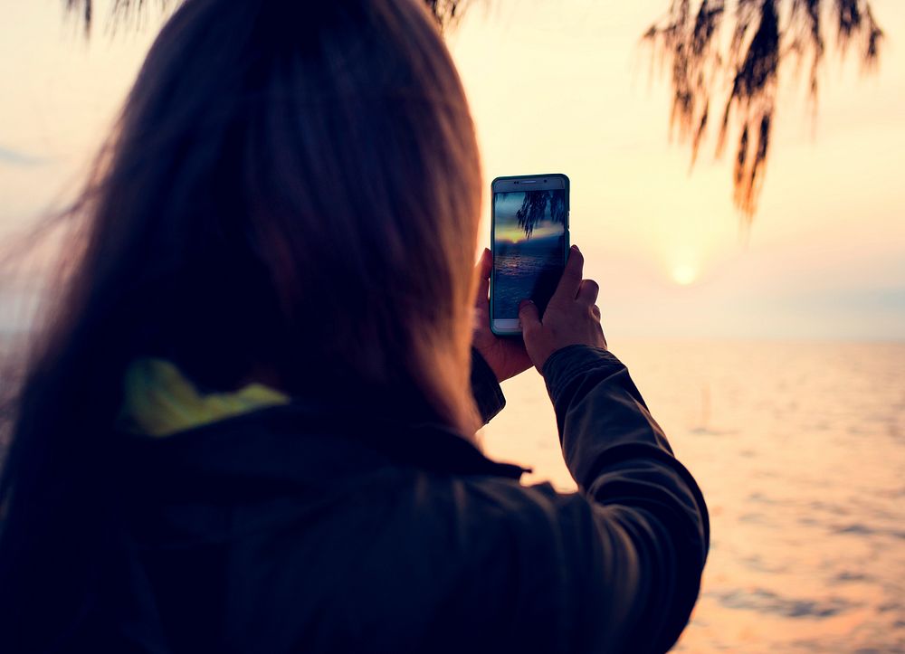 Girl taking photo of the sunset with her mobile phone