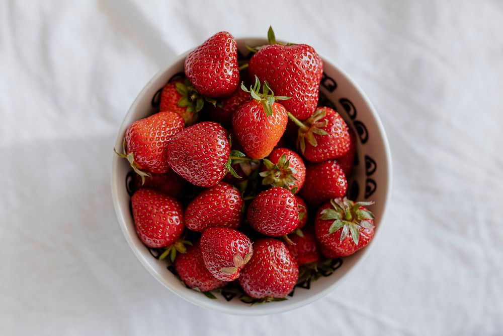 Freshly harvested strawberries in a white bowl flatlay