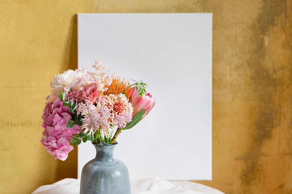 Blank board mockup against a yellow wall by a vase of flowers