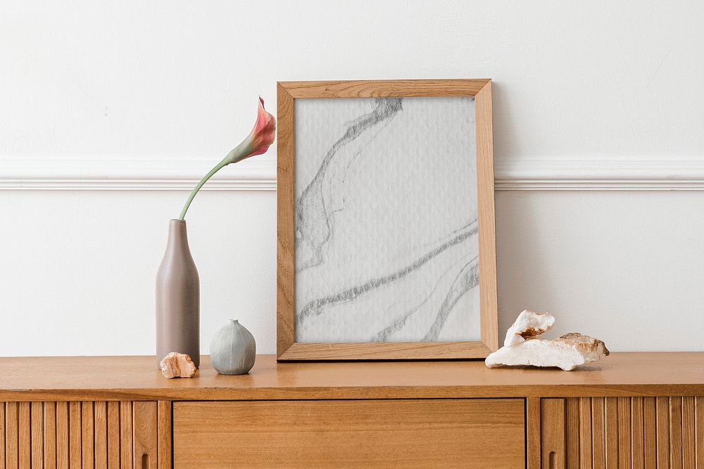 Picture frame mockup on a wooden sideboard table with a flower in a vase 