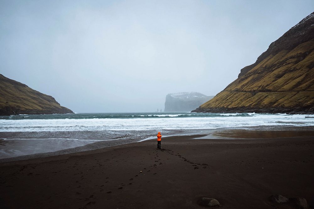 Woman in an orange windbreaker at Tj&oslash;rnuv&iacute;k beach in the Faroe Islands