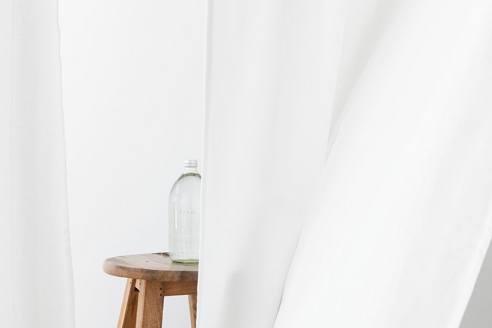 Glass water bottle on a wooden stool behind a flowing white curtain
