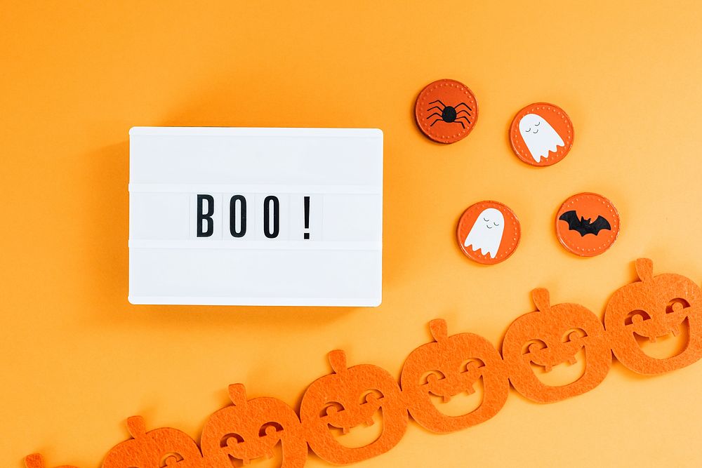 Boo on a white letter board by a pumpkin garland 