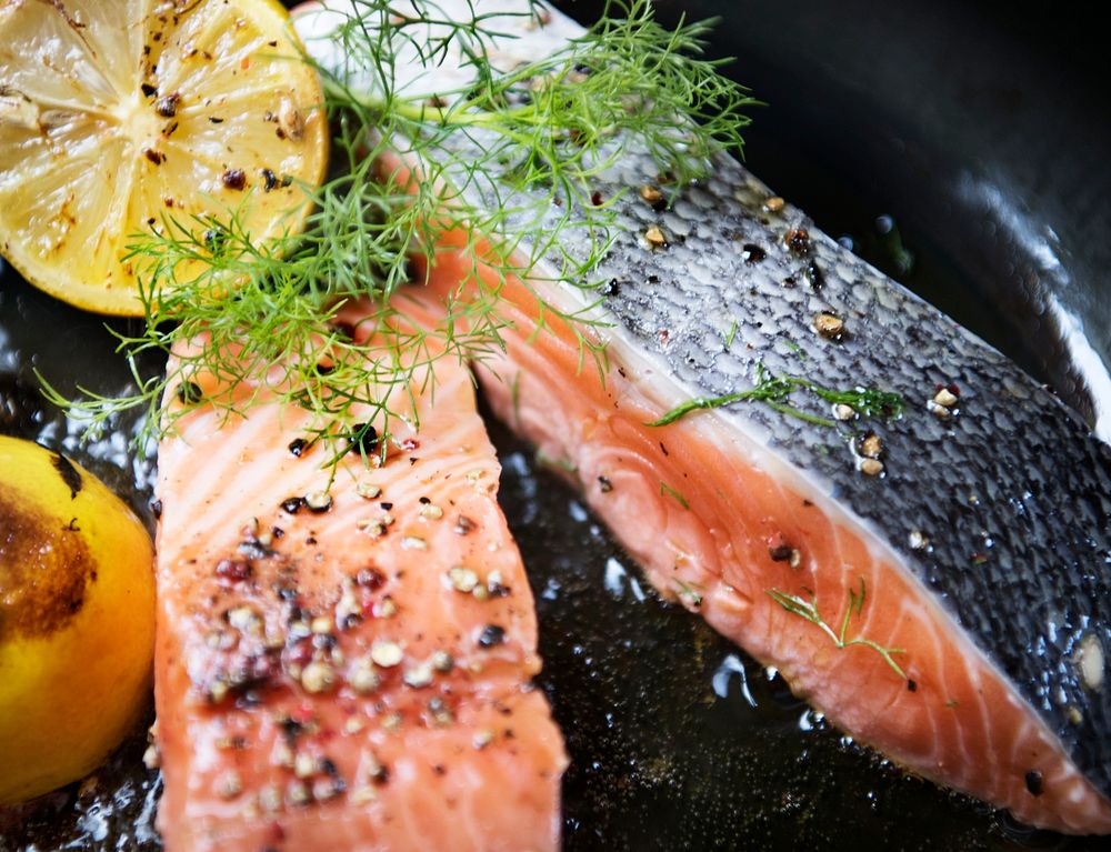 Grilled salmon fillet being sprinkled with salt and pepper