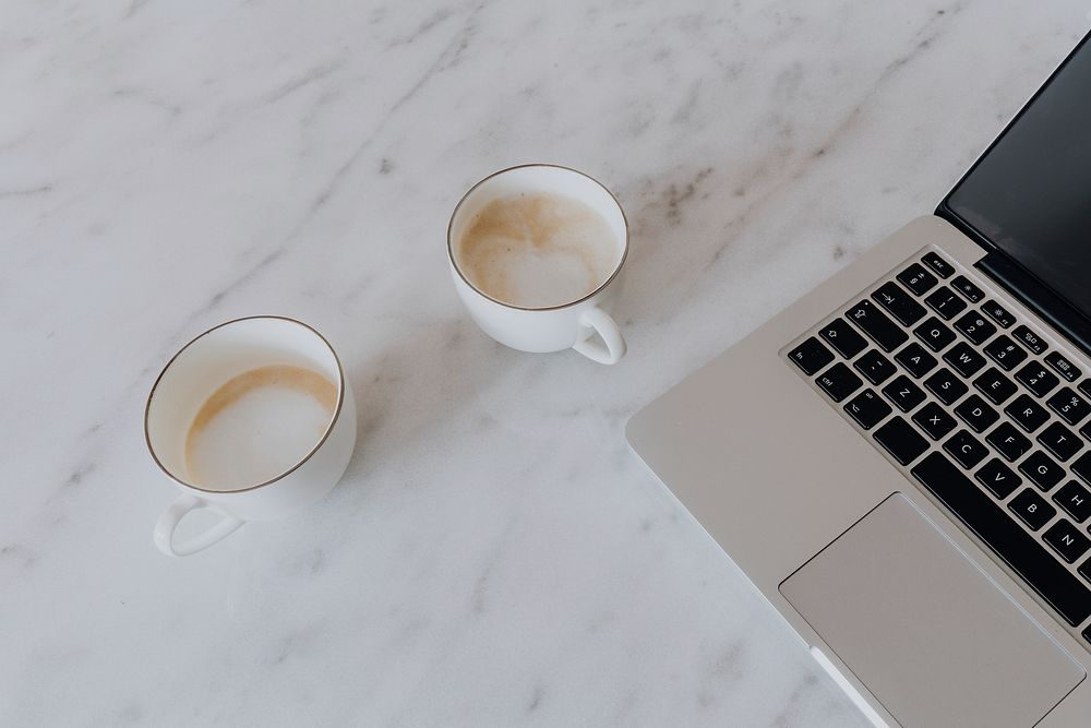 Two cups of latte and a laptop on a marble table