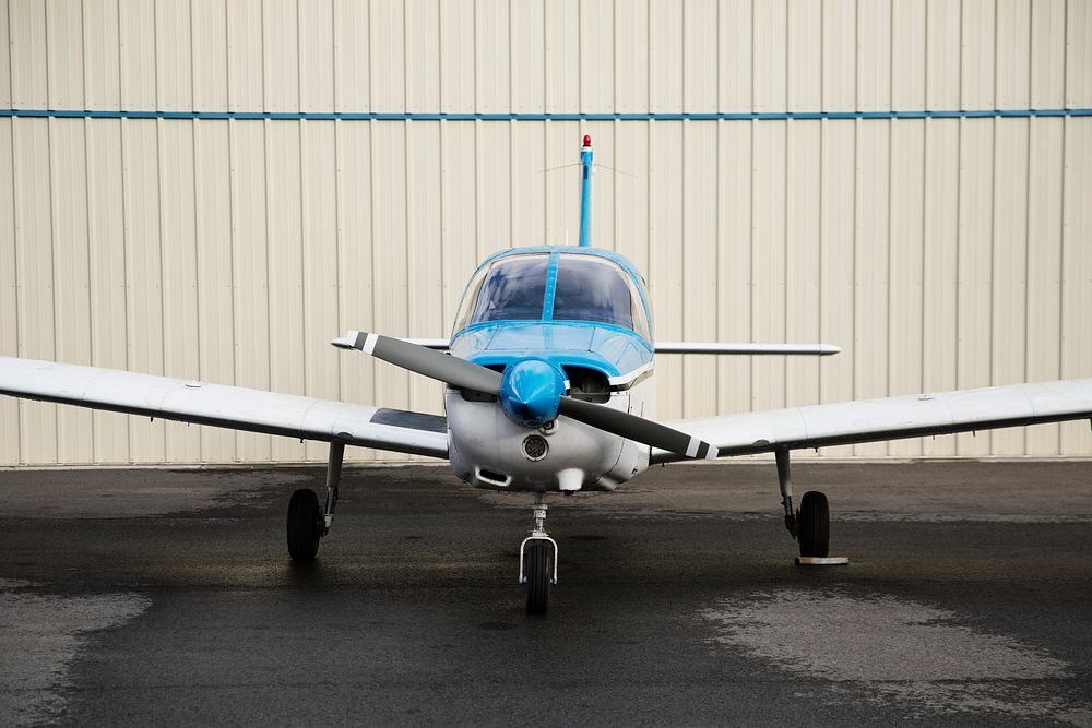 Blue front propellor plane outside a hangar