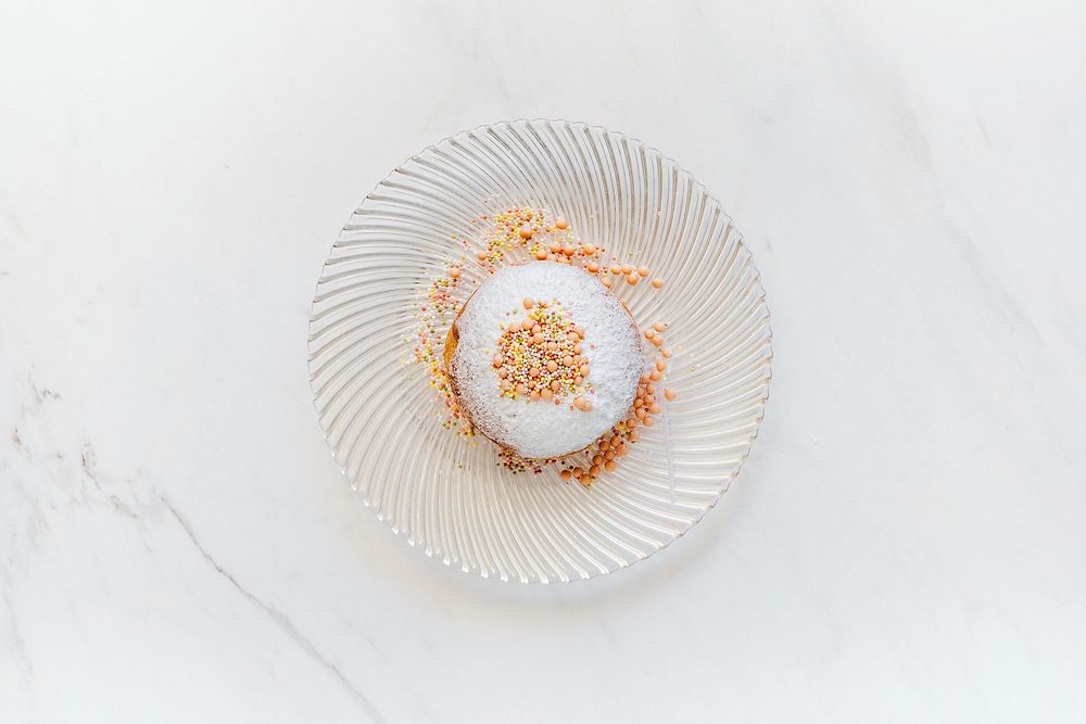 Donut decorated with sprinkles served on a white marble table
