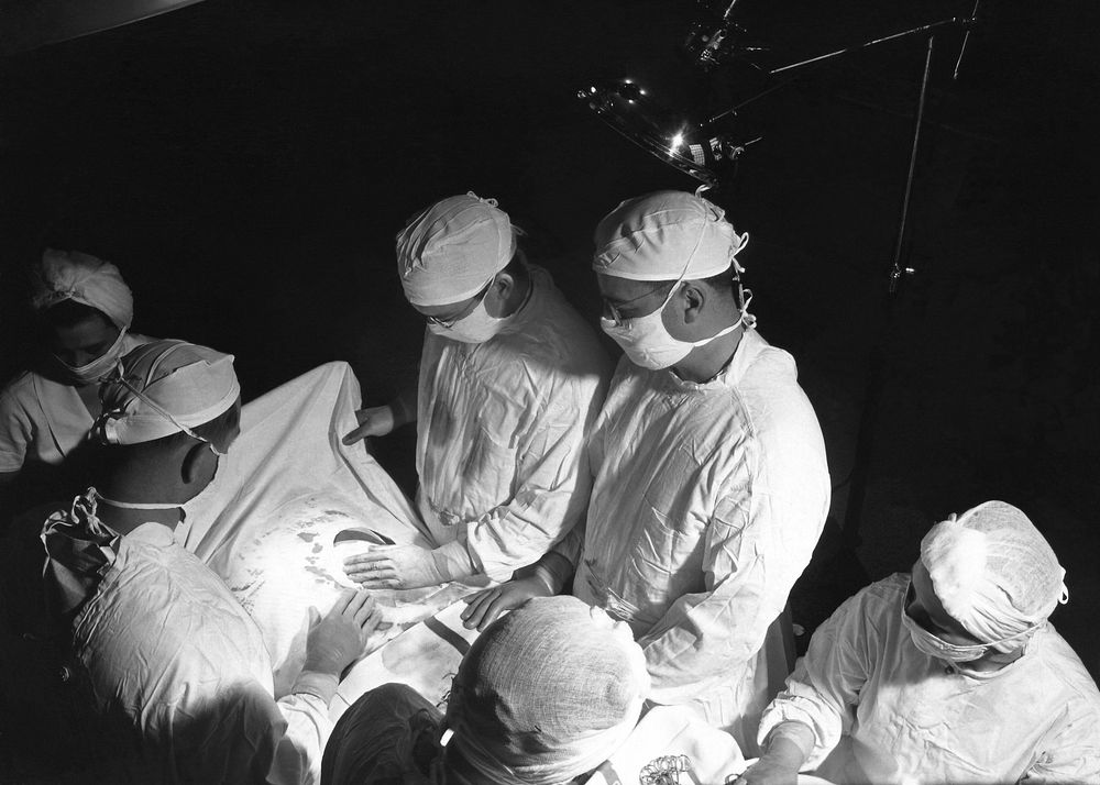 The 1950s historical photograph of the inside of an operating room suite during a surgical procedure.