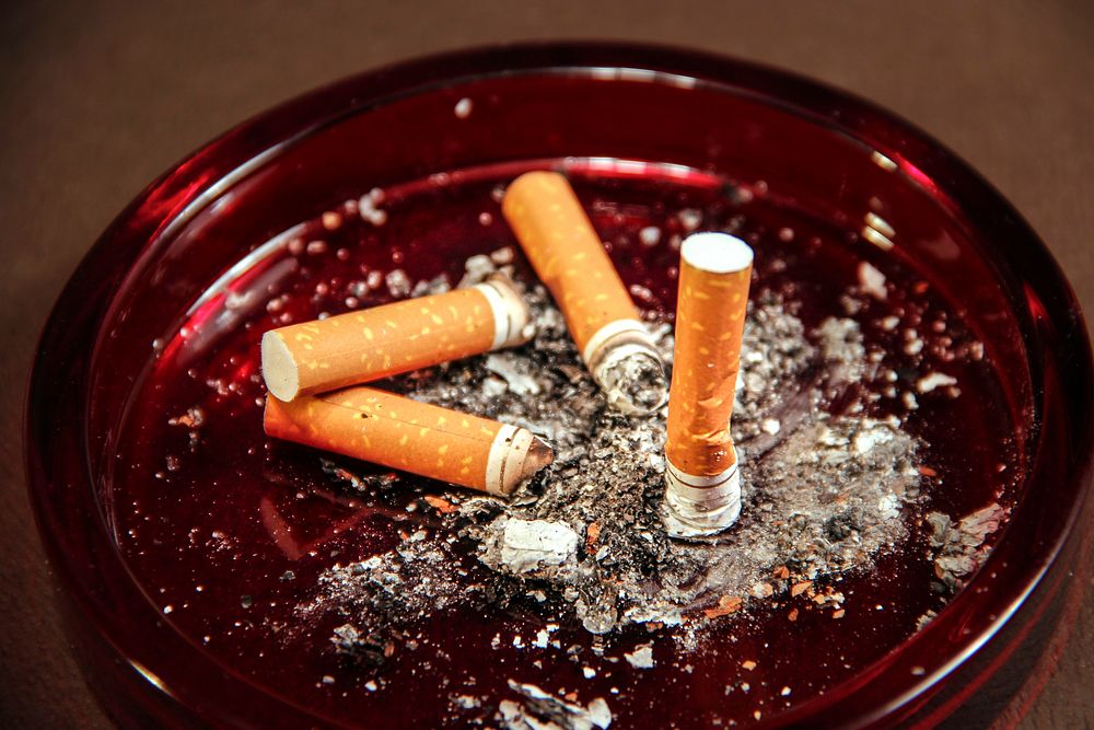 An amber&ndash;colored glass ashtray filled with used cigarette butts along with their ashes.