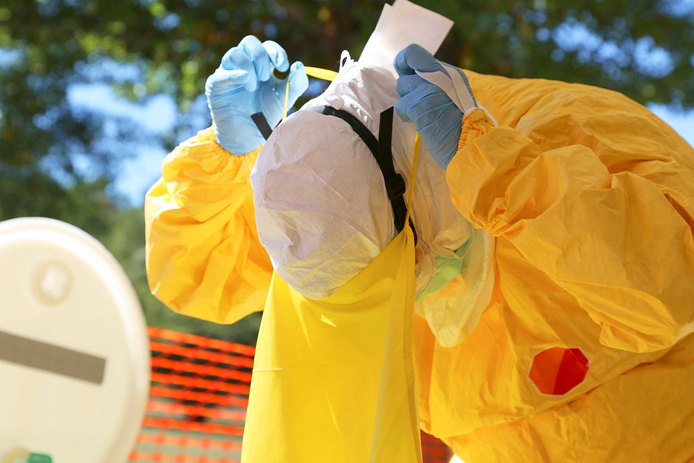 Healthcare worker donning the final article of personal protective equipment (PPE), a plastic apron, which would complete…
