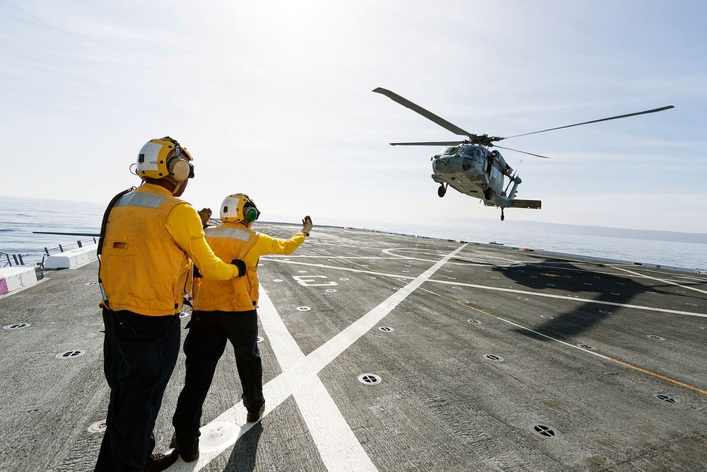 On the top deck of the USS San Diego, U.S. Navy personnel monitor a helicopter landing. Original from NASA. Digitally…