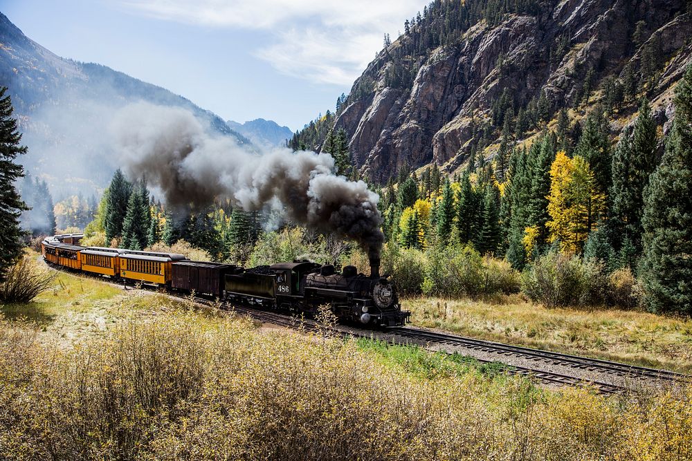 Scenic Railroad train, pulled by a vintage steam locomotive, chugs through the San Juan Mountains in the Colorado county of…