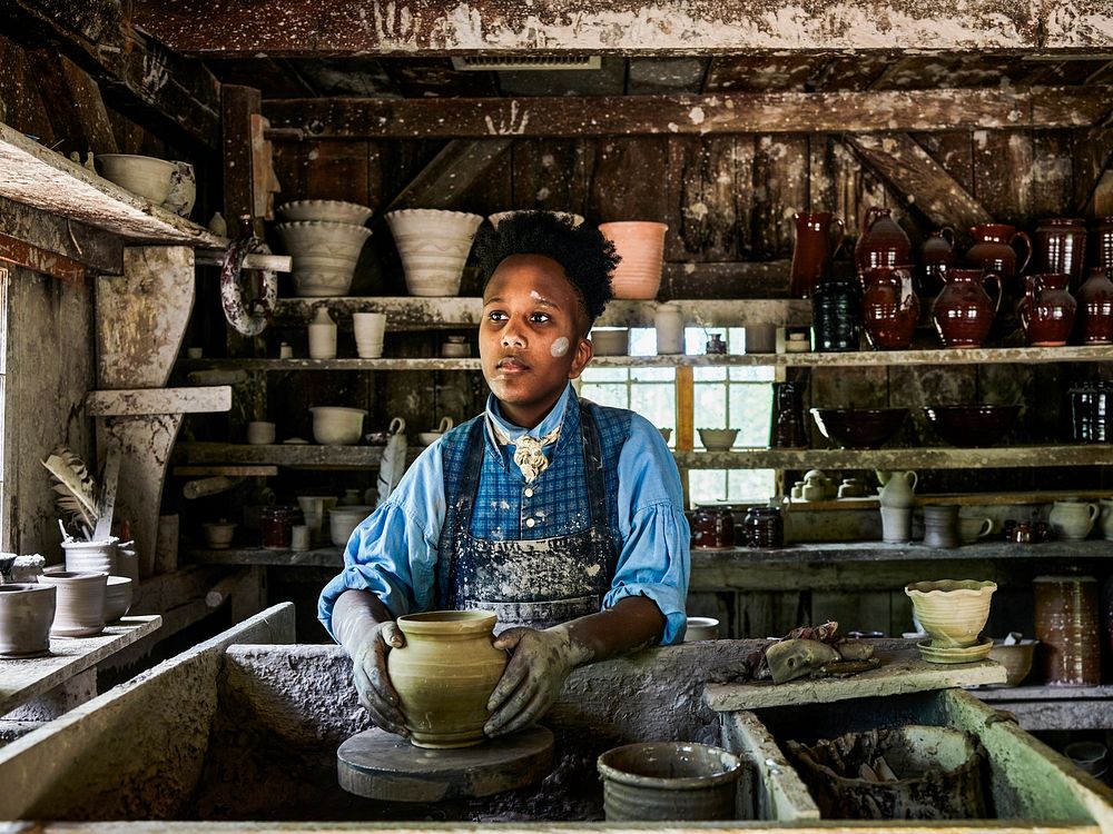 Costumed man works in the pottery shop at Old Sturbridge Village, New England&rsquo;s largest outdoor living-history museum…