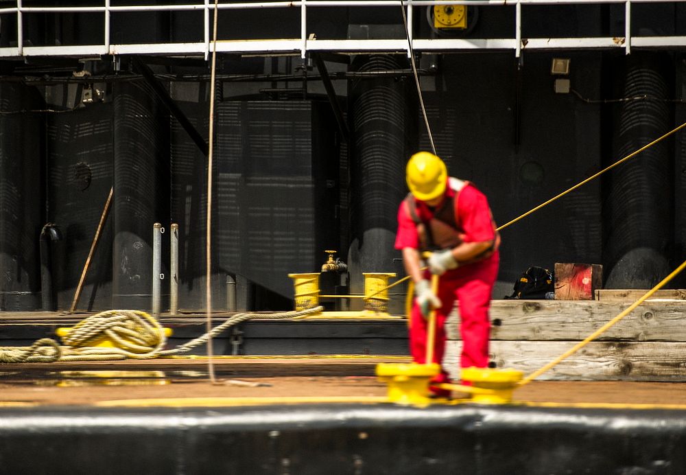 Workers control support ropes from the space shuttle Enterprise to lift it off of a barge and onto the Intrepid Sea, Air and…