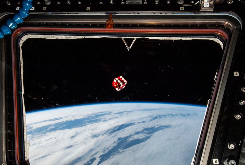 A dice floating in front of one of the windows in the Cupola of the Earth-orbiting International Space Station. Original…