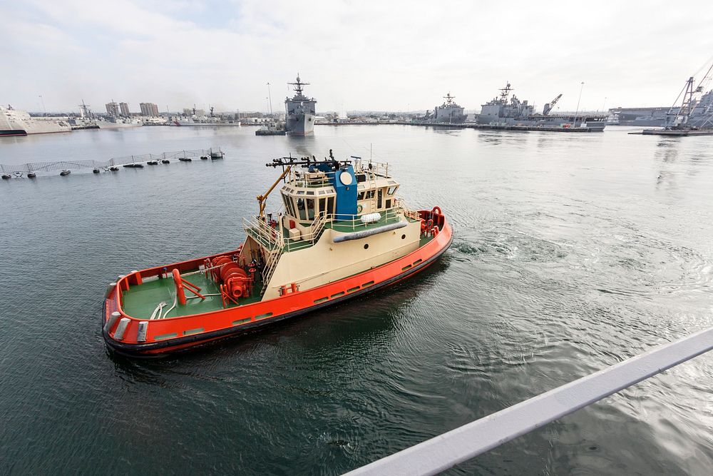 At the U.S. Naval Base San Diego in California, a tug boat accompanies the USS San Diego as it departs for open seas in the…