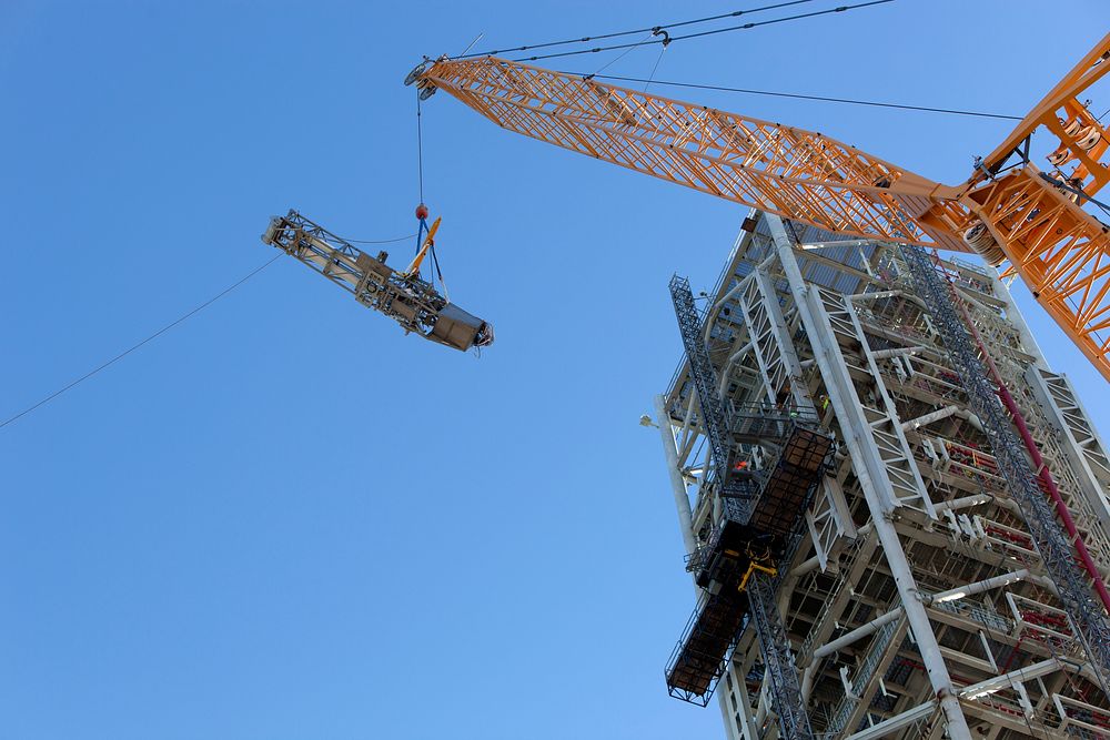 A crane and rigging are used to lift the Orion Service Module Umbilical (OSMU) high up for installation on the mobile…