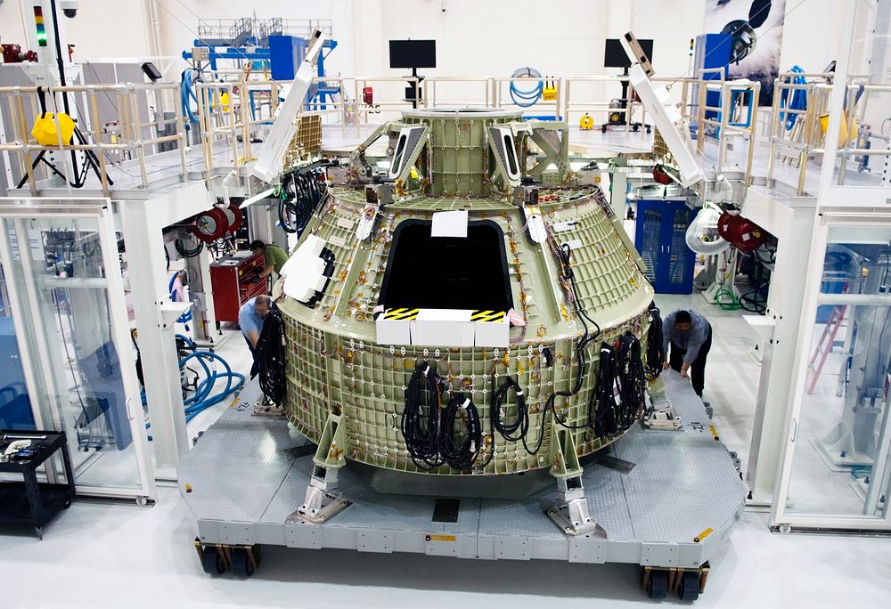 Technicians prepare to fit a special fixture around an Orion capsule inside the high bay of the Operations & Checkout…