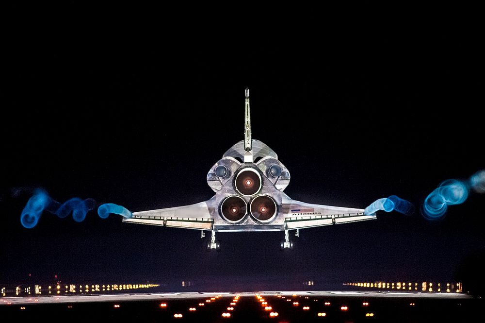 Vapor trails follow space shuttle Atlantis as it approaches Runway 15 on the Shuttle Landing Facility at NASA's Kennedy…