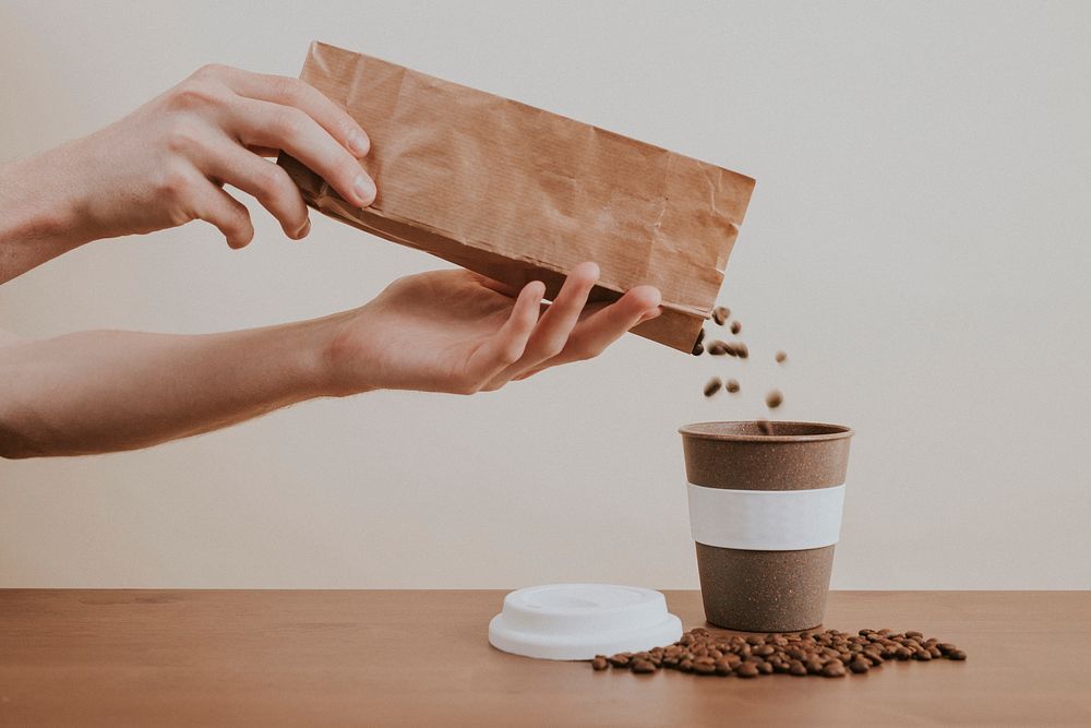 Hand pouring coffee beans from a paper bag into a coffee cup