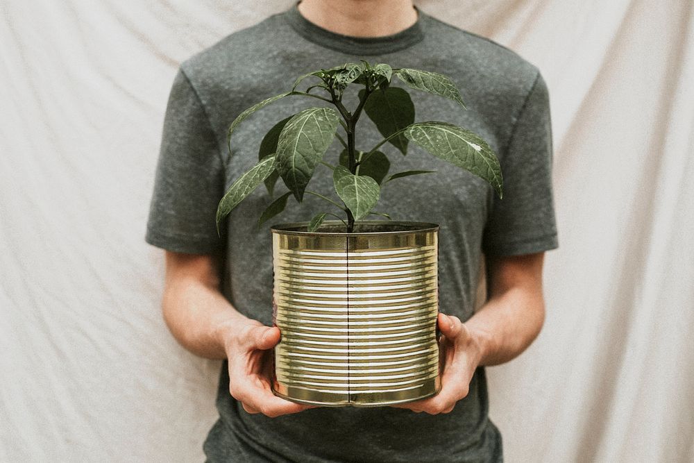 Man in a green t-shirt holding plant in a tin can pot