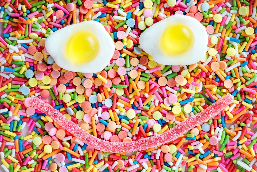 Flatlay of jelly fried eggs forming a smiley face and sprinkles textured background
